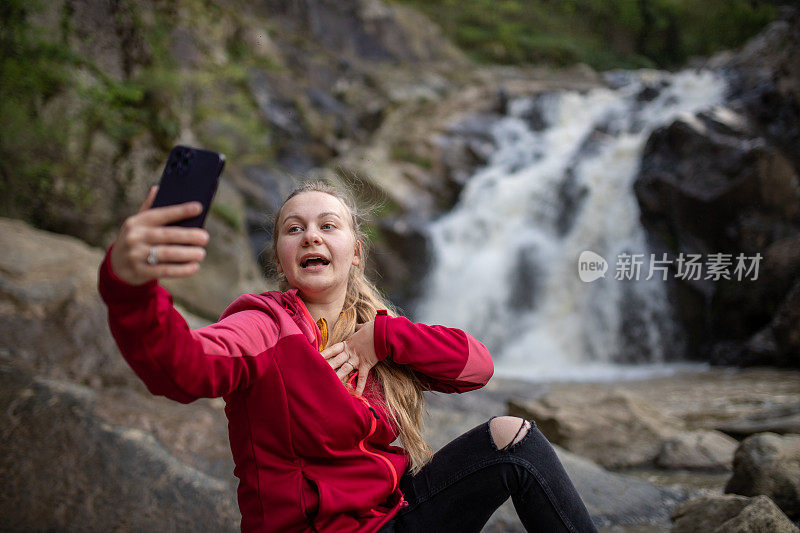 年轻的徒步旅行者在大自然中用她的智能手机为她的粉丝打视频电话/录制视频